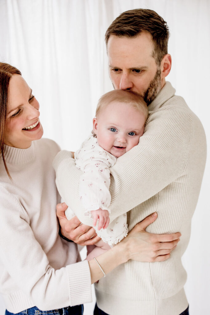 Mum Dad and Baby cuddling and kissing baby 