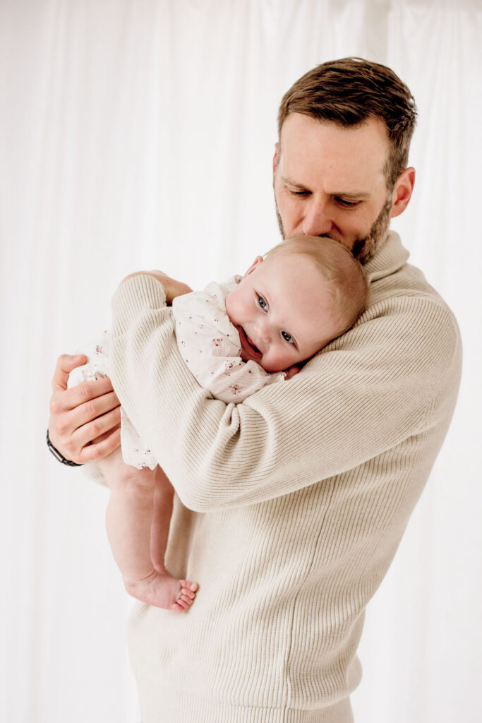 Father holding and kissing 6 month old baby for family photography session